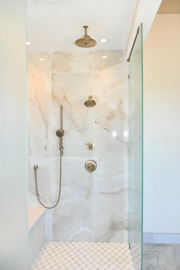 Modern walk-in shower with marble-look tile, glass panels, rainfall showerhead and handheld shower fixtures